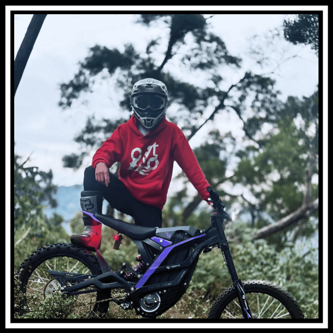 A rider in a red hoodie and helmet poses on a 79BIKE-FALCON PRO 10000W OFF-ROAD electric dirt bike.