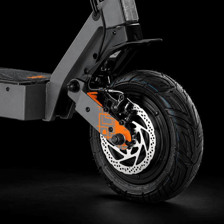 Kukirin G4 Ultra Electric Scooter - Close-up of a black electric scooter wheel with a silver disc brake, black tire, and bright orange front fork accent against a dark studio background.