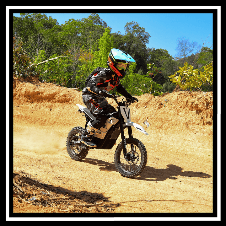 Rider on a VIPCOO H2 electric dirt bike navigating an off-road trail with greenery in the background.