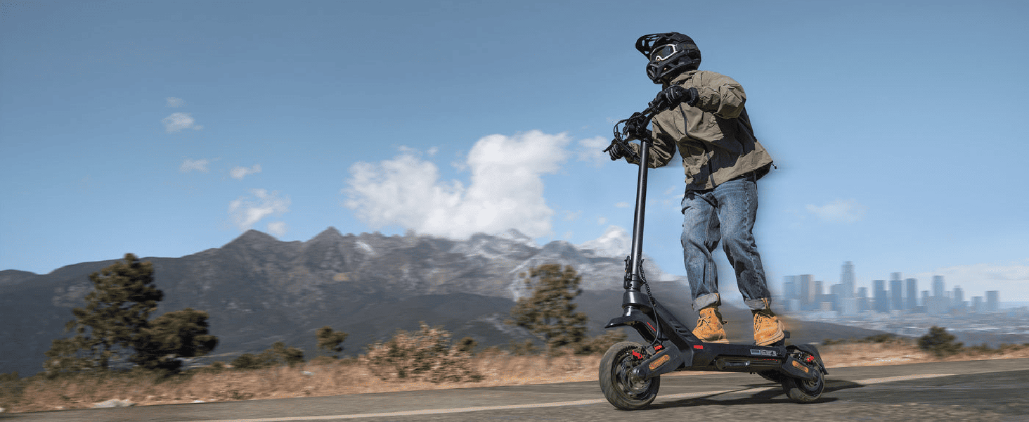 Person riding an electric scooter on a scenic road with mountains in the background.