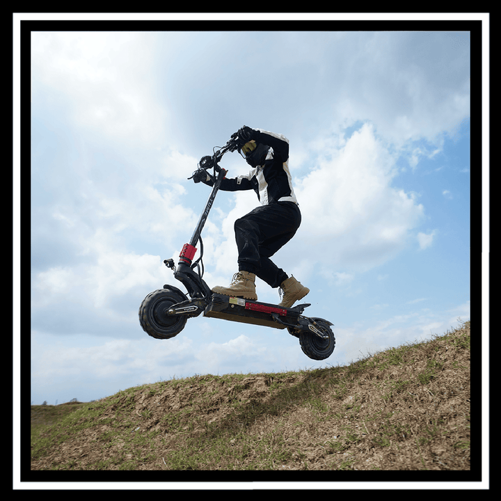 Rider jumping on YUME Raptor 2 electric scooter on a grassy hill under blue sky.
