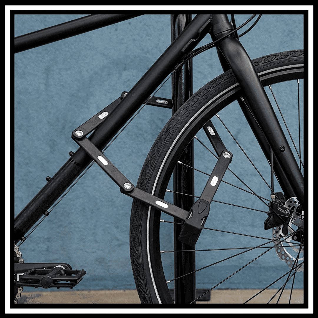 🇮🇪🇪🇺 ABUS BORDO BIG 6000K/90/120 folding lock secured to a black bicycle wheel against a blue wall.