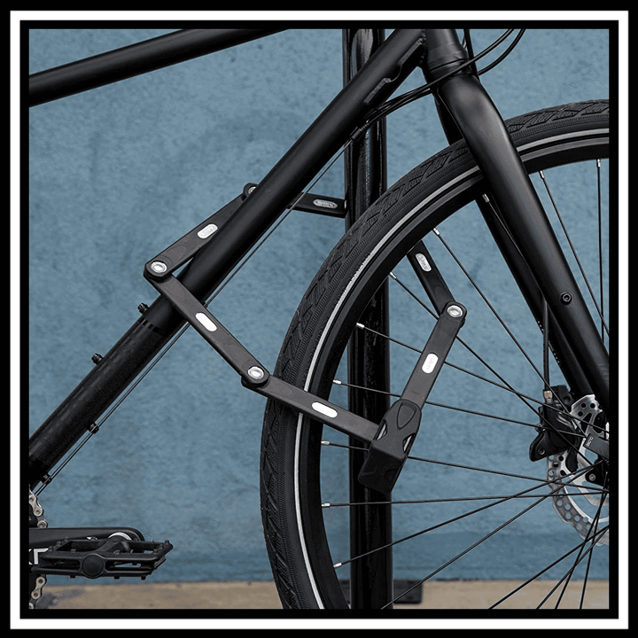 🇮🇪🇪🇺 ABUS BORDO BIG 6000K/90/120 folding lock secured to a black bicycle wheel against a blue wall.