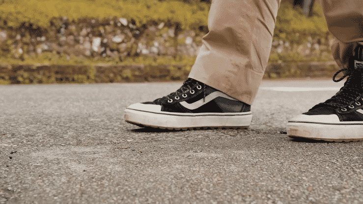 A close-up of a person wearing black and white sneakers walking on a road.