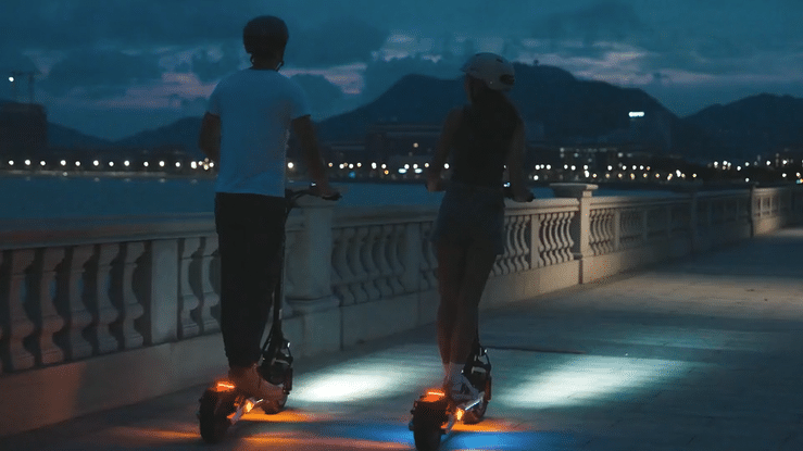 KUKIRIN M4 MAX ELECTRIC SCOOTER riders enjoying a nighttime ride along a scenic waterfront pathway.
