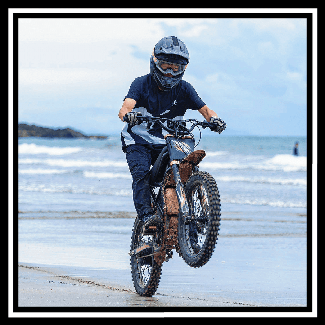 Rider performing a wheelie on the GT73 2400W RIDING' TIMES DIRT E-BIKE at the beach.