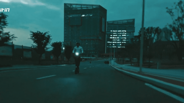 A rider using the 🇮🇪🇪🇺 KUKIRIN G2 electric scooter at night on an urban road with buildings in the background.