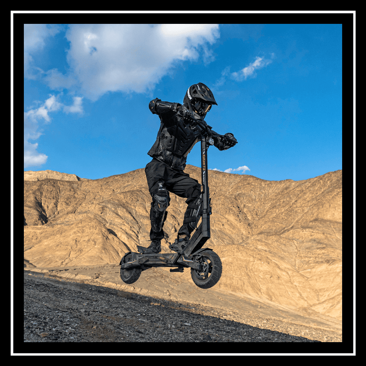 A person riding the 🇮🇪🇪🇺 KUKIRIN T3 ELECTRIC SCOOTER jumps on a rugged terrain against a mountain backdrop.