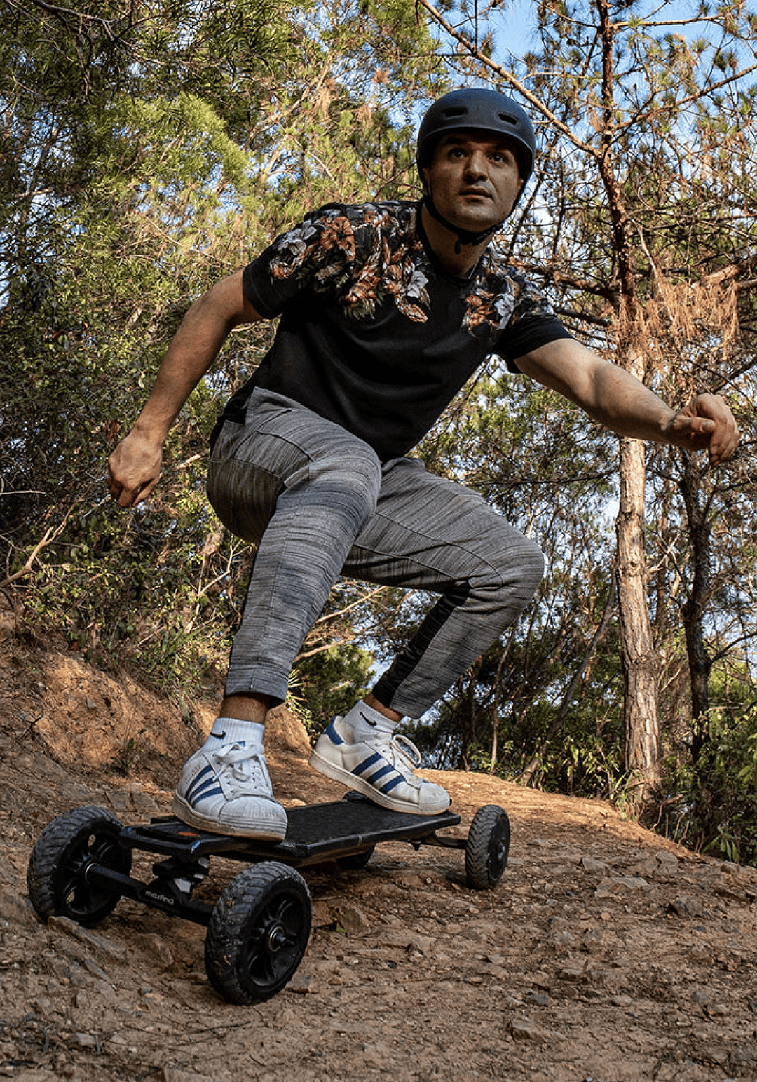Rider performing a stunt on a Maxfind FF AT electric skateboard in a wooded area, showcasing its off-road capabilities.