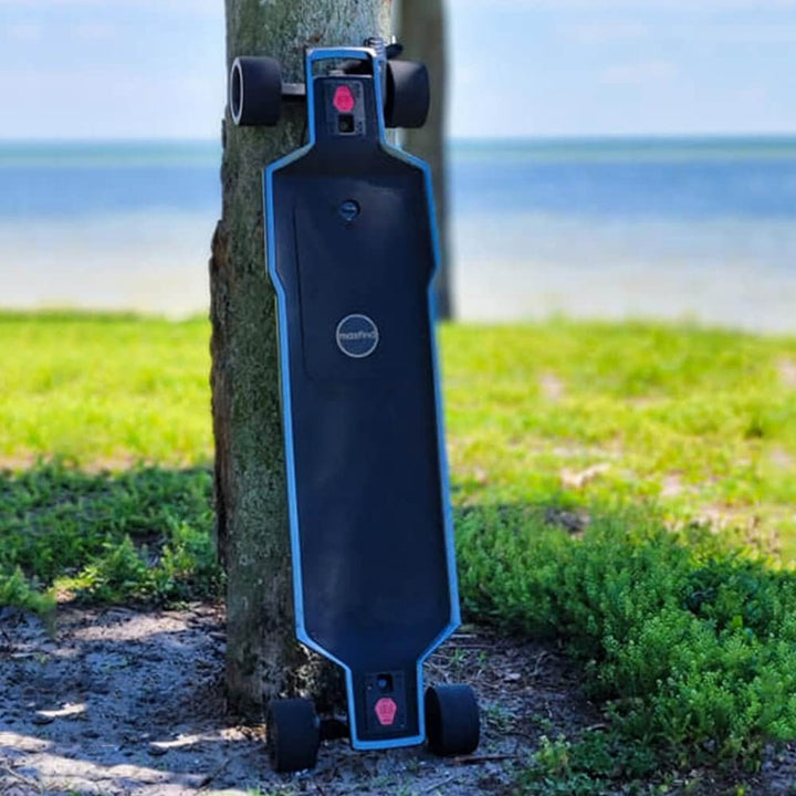 MAXFIND FF PRO electric skateboard leaning against a tree near a scenic waterfront.