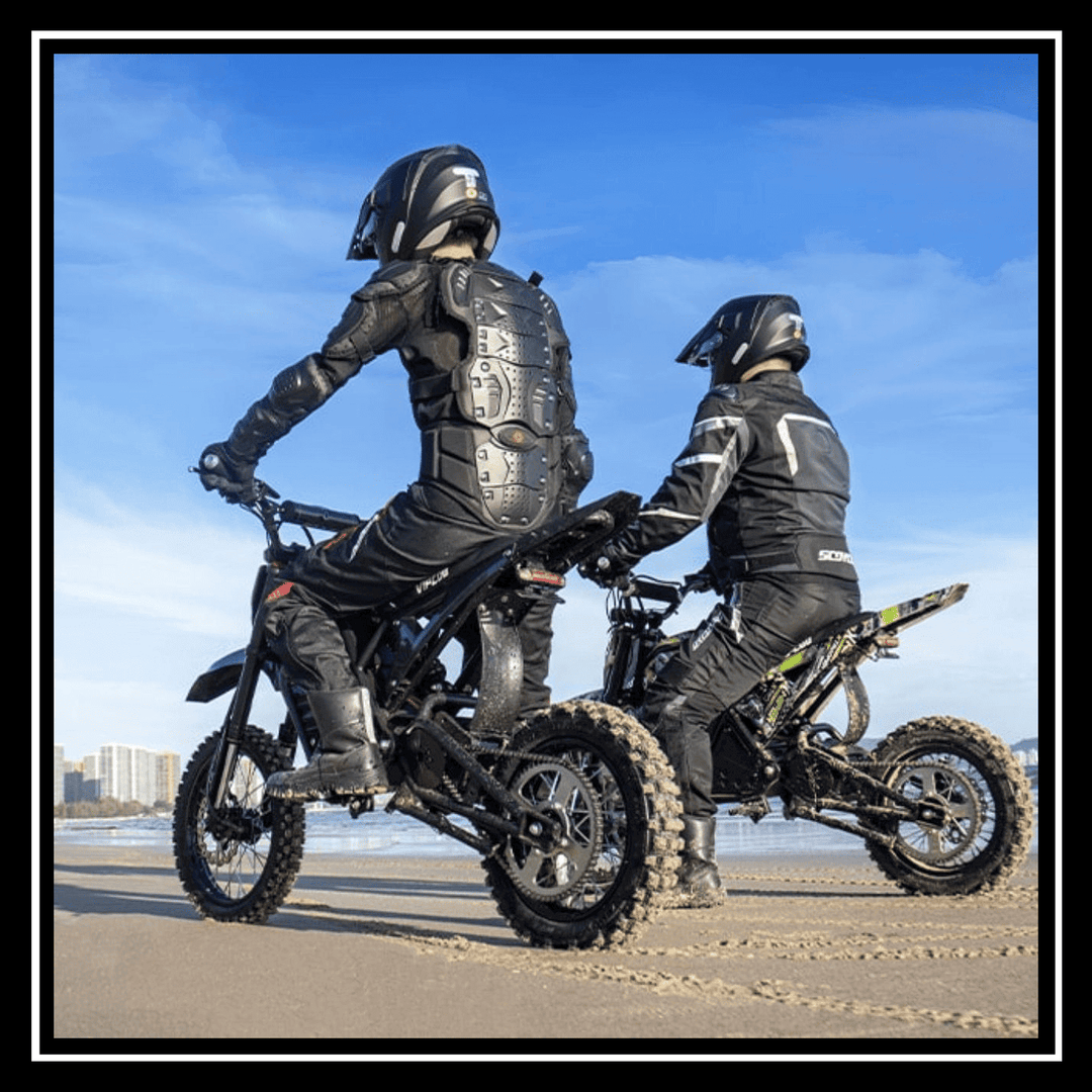 Two riders on VIPCOO H3 3500W E-DIRT BIKE at the beach under a blue sky.