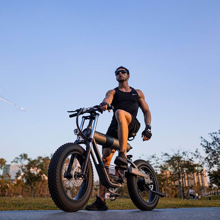 Man riding the COSWHEEL T20 electric bike in an outdoor park during sunset.