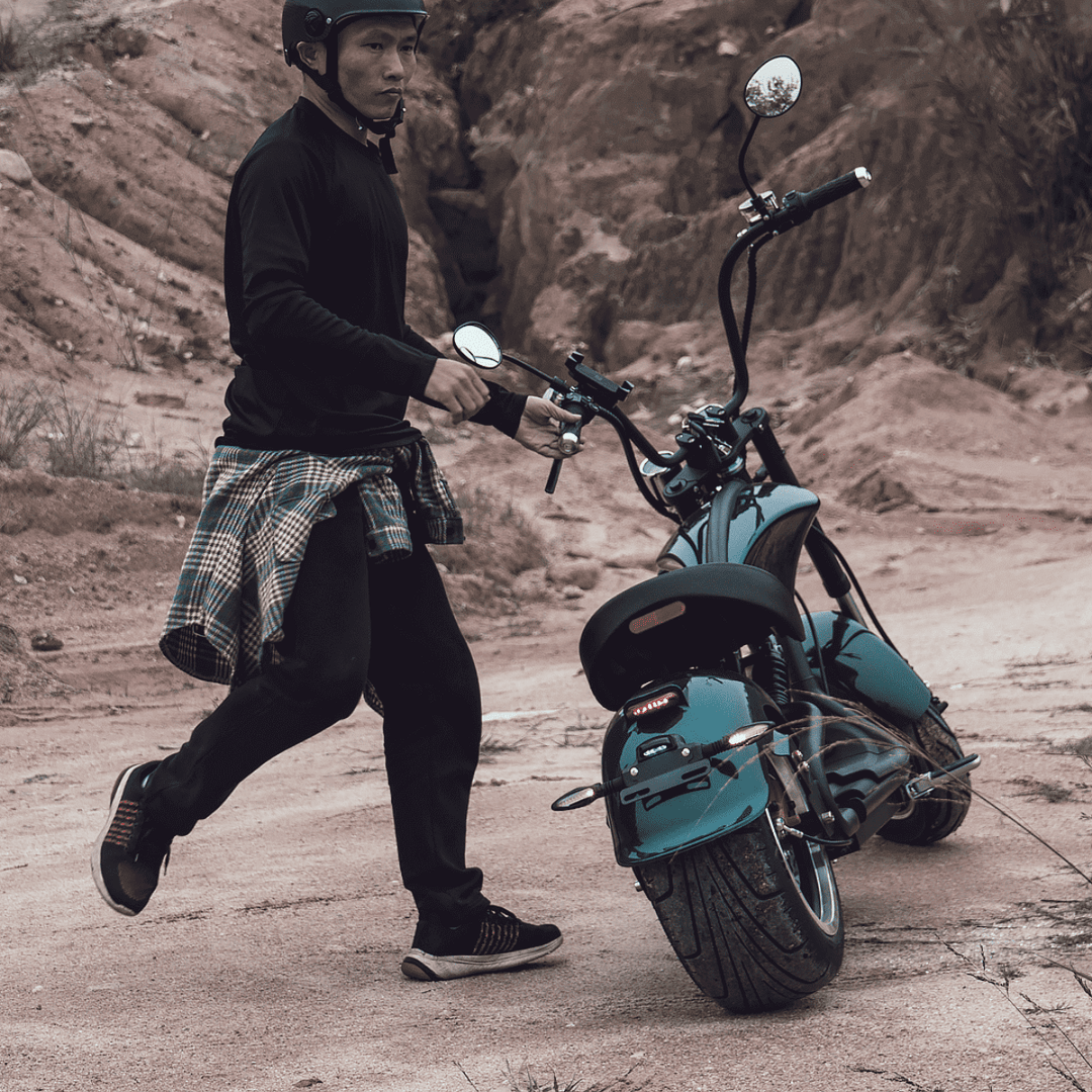 Man walking alongside EAHORA M1P PLUS electric motorcycle in rugged outdoor terrain.