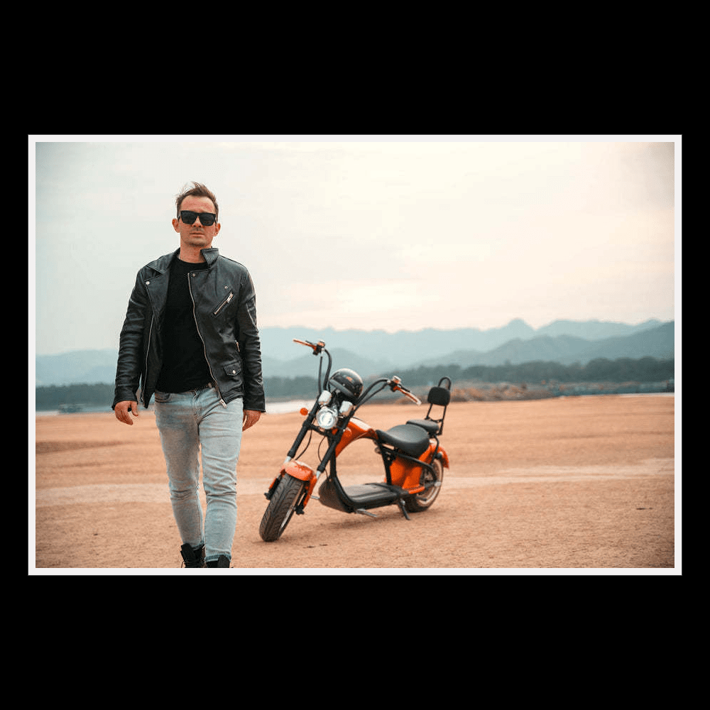 EAHORA MP1 two-seat electric motorcycle with rider in stylish leather jacket walking on sandy terrain.