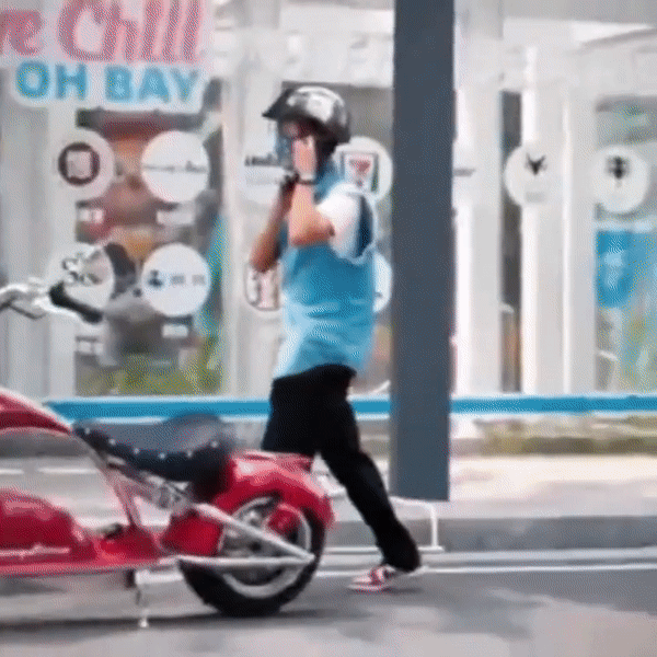 Person wearing a helmet and blue shirt preparing to ride the INTHEZONE M1PS electric motorcycle in an urban setting.