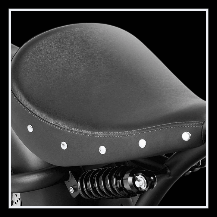 Detailed view of the black seat of the INTHEZONE M1PS electric motorcycle showing chrome studs and suspension.