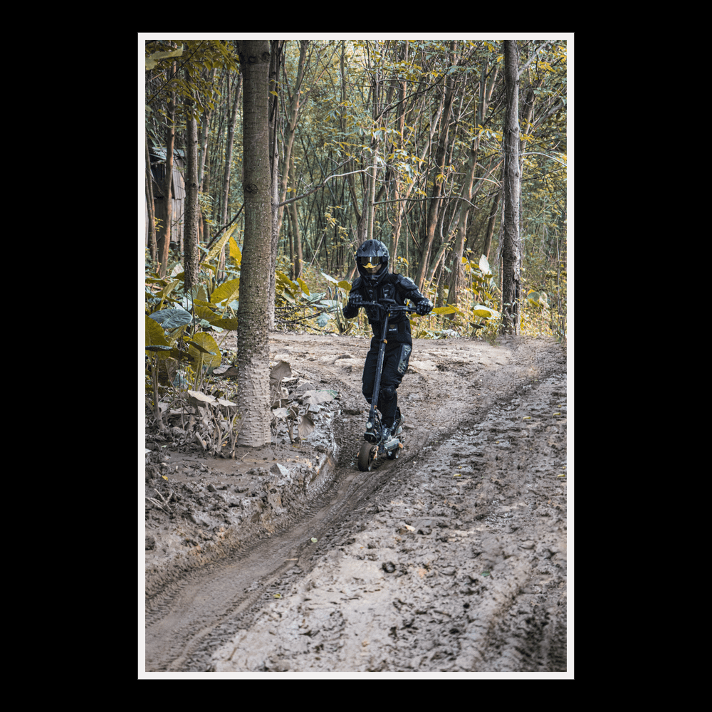 Rider using KUKIRIN G2 Pro electric scooter on a muddy trail in a forest setting.