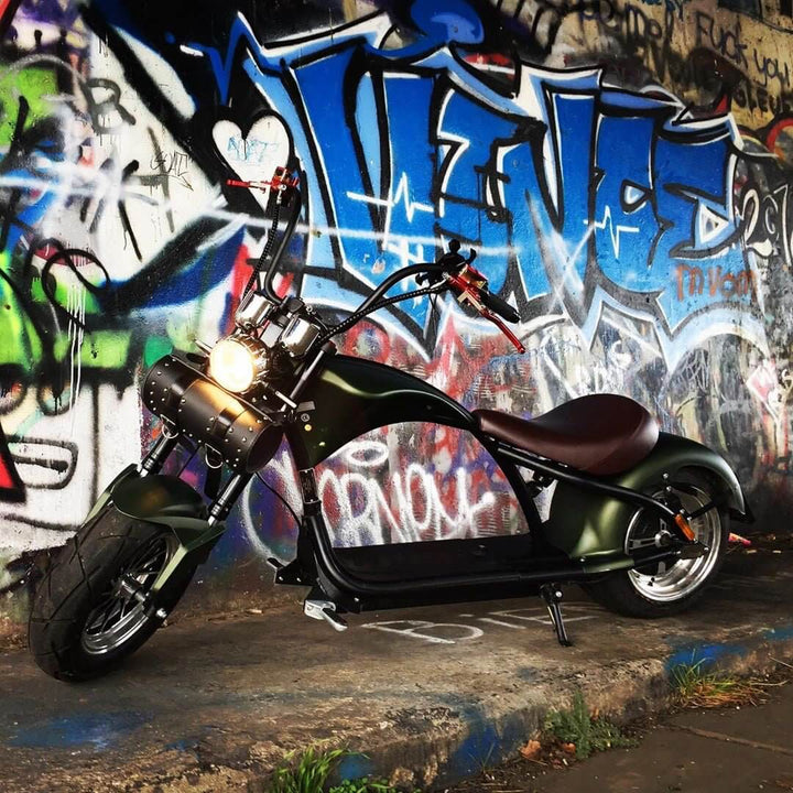 M1P electric chopper motorcycle parked against a vibrant graffiti wall, showcasing its stylish Harley-style design.