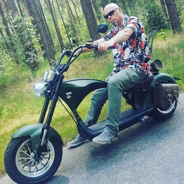 M1P electric chopper motorcycle being ridden in a forested area, showcasing its Harley-style design and features.