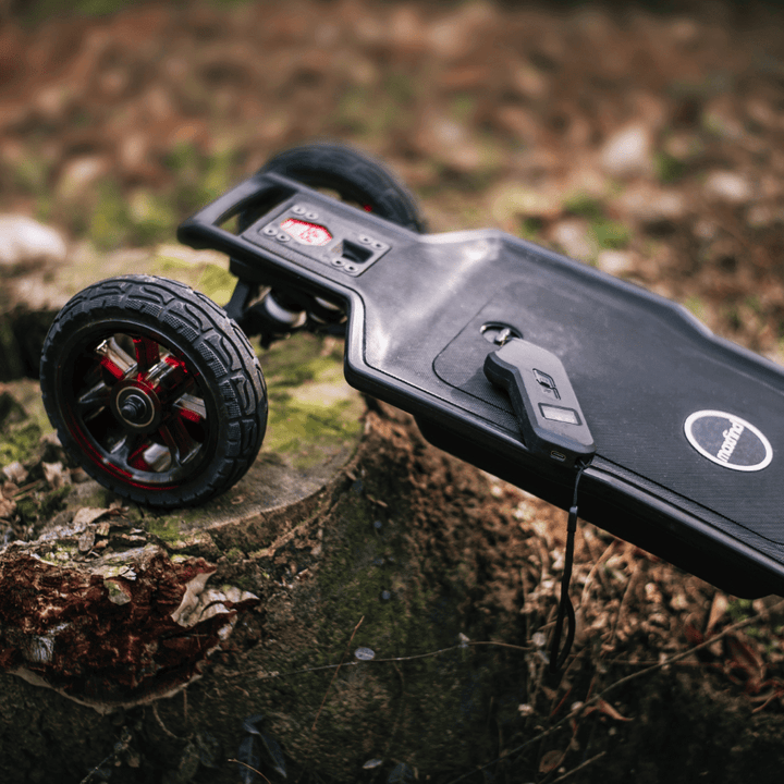 Maxfind FF AT electric skateboard resting on a log with large all-terrain wheels and a remote control.