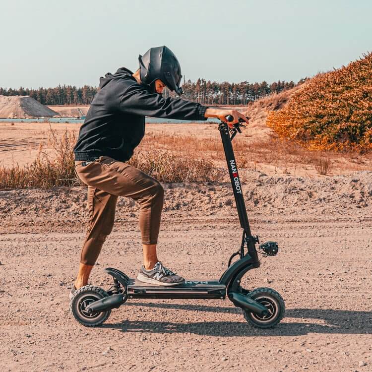 Person riding a Nanrobot D6+ electric scooter on a dirt path, showcasing its off-road capability and design.