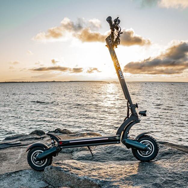 Nanrobot D6+ electric scooter on rocky shore at sunset, showcasing its sleek design and off-road capability.