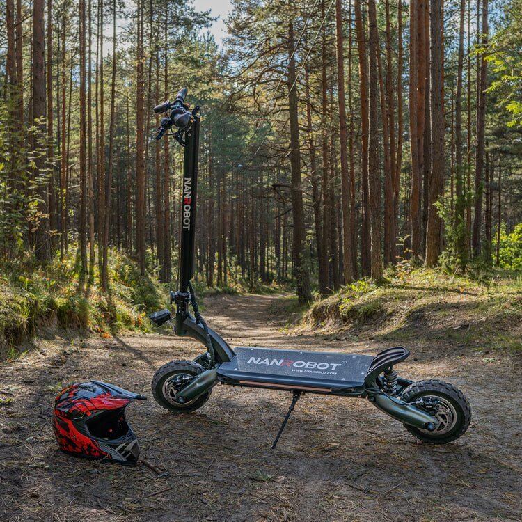Nanrobot D6+ electric scooter parked on a forest trail with a helmet beside it.